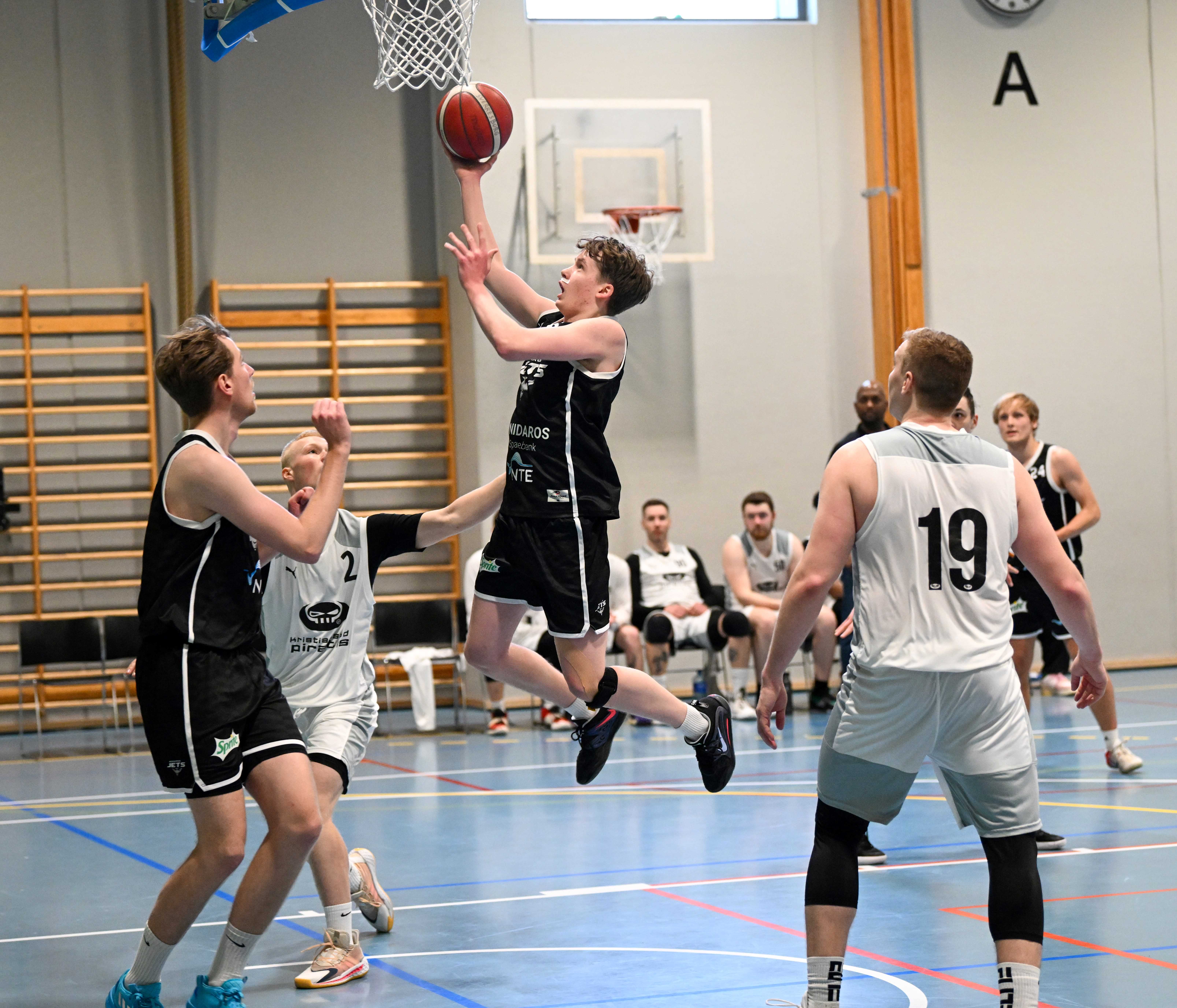 19-årige Tobias Edvardsen Øvermo har brutt gjennom Kristiansand Pirates' forsvar og går på layup i søndagens kamp, der Nidaros Jets vant 76-47. Tor Anders Ringen (til venstre) er klar for eventuell retur, Kristiansands forsvarsspillere er Girts Iljins (nr 2) og Anders Iam Ham. Bak til høyre ser vi Arne Marius Grevskott.
FOTO: LARS RUNE SKAUG 