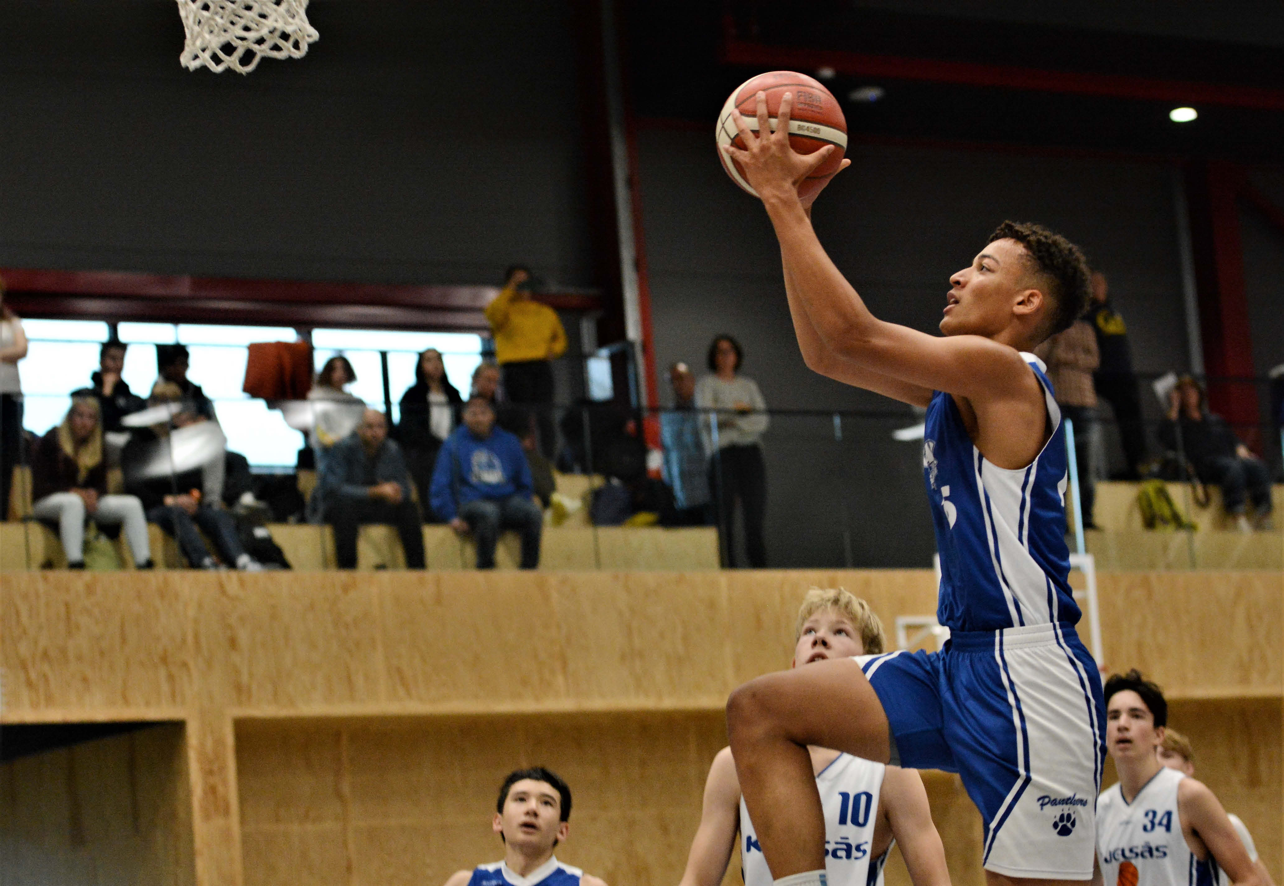 Etienne Nasser Aspevik svever høyt og legger to poeng for Oppsal i G05-finalen. Oppsal ledet med 6 poeng i andre omgang og stillingen var 48-48 med 20 sekunder igjen å spille, men Kjelsås fikk inn de avgjørende scoringene og vant 51-48. De øvrige spillerne på bildet er fra venstre Oppsals David Ayden og Kjelsås' Sivert Wærstad Nordheim (nr 10) og Andrej Grubor (nr 34).
FOTO: MARIANNE MAJA STENERUD  