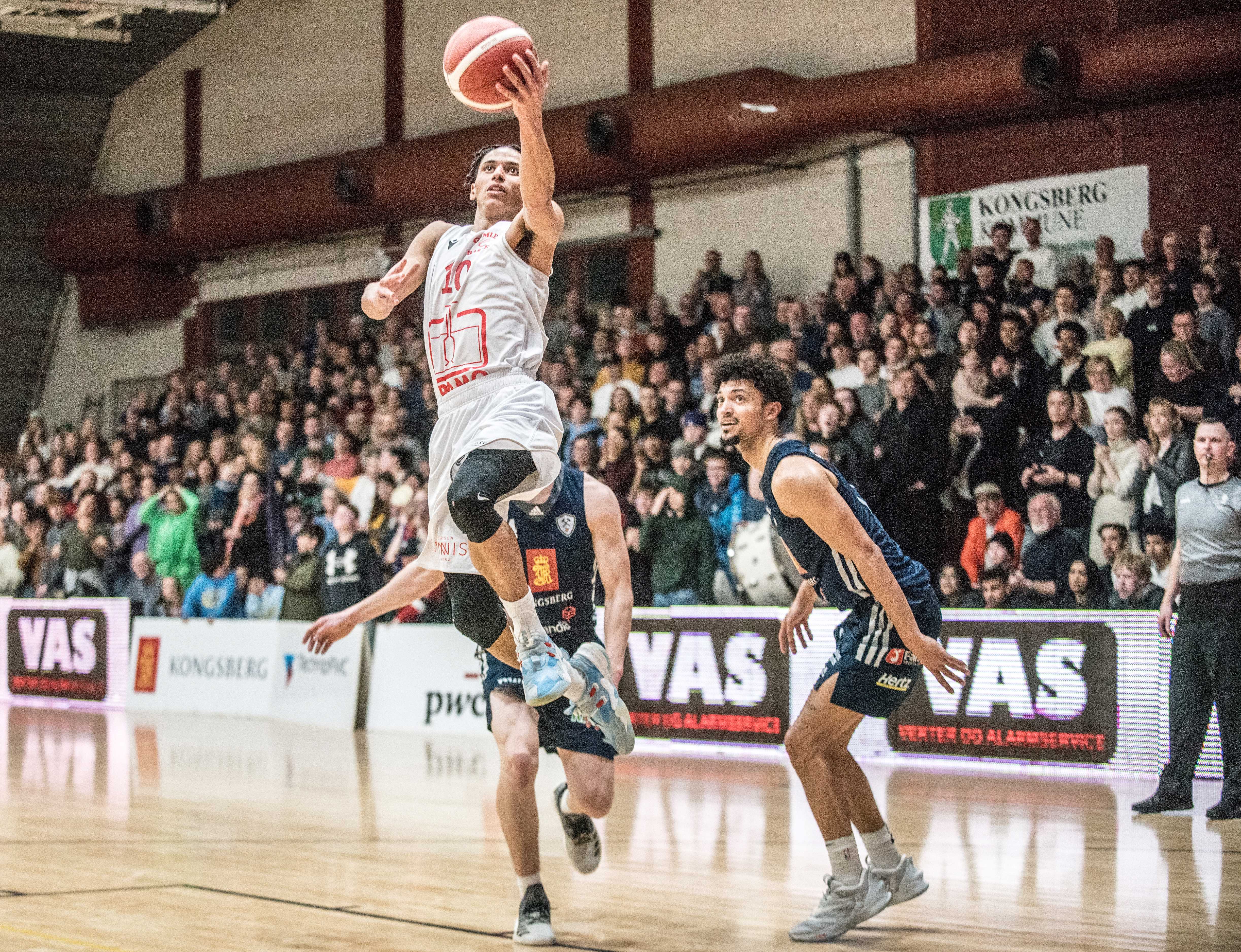 Lars Fredrik Espe skjøt, drivet og ble toppscorer med 23 poeng da Gimle slo Kongsberg Miners 80-68 og sikret finaleplass. Her er bergensernes pointguard på vei til ny scoring, forbi Matias Save (skjult) og Bryan Alberts. Til høyre er dommer Mantas Buinauskas.
FOTO: ERIK BERGLUND