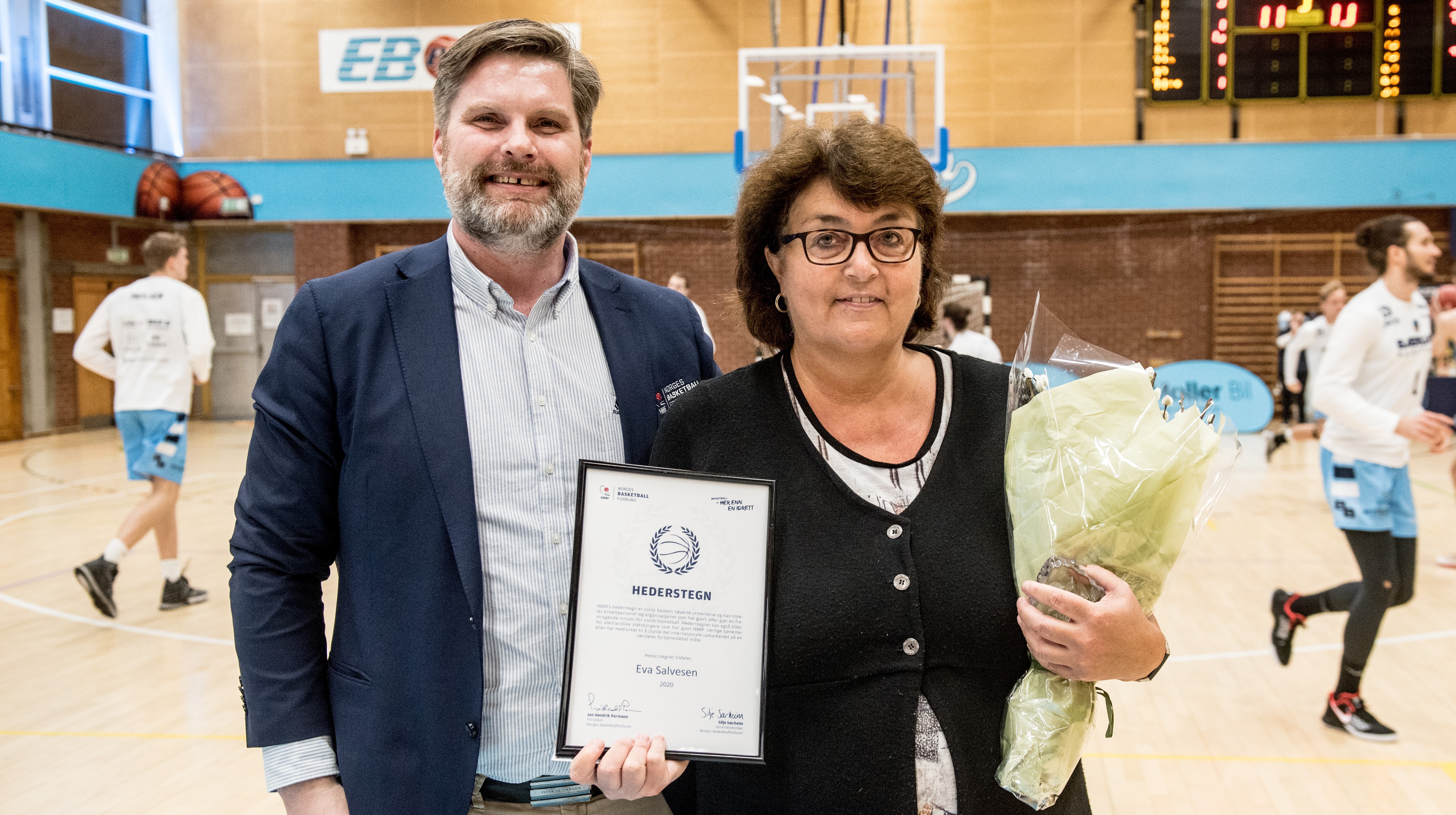 Eva M. Salvesen med NBBFs Hederstegn og blomsterbuketten hun mottok fra basketballpresident Jan Hendrik Parmann i pausen i tirsdagens BLNO-kvartfinale mellom Bærum og Centrum Tigers. FOTO: ERIK BERGLUND