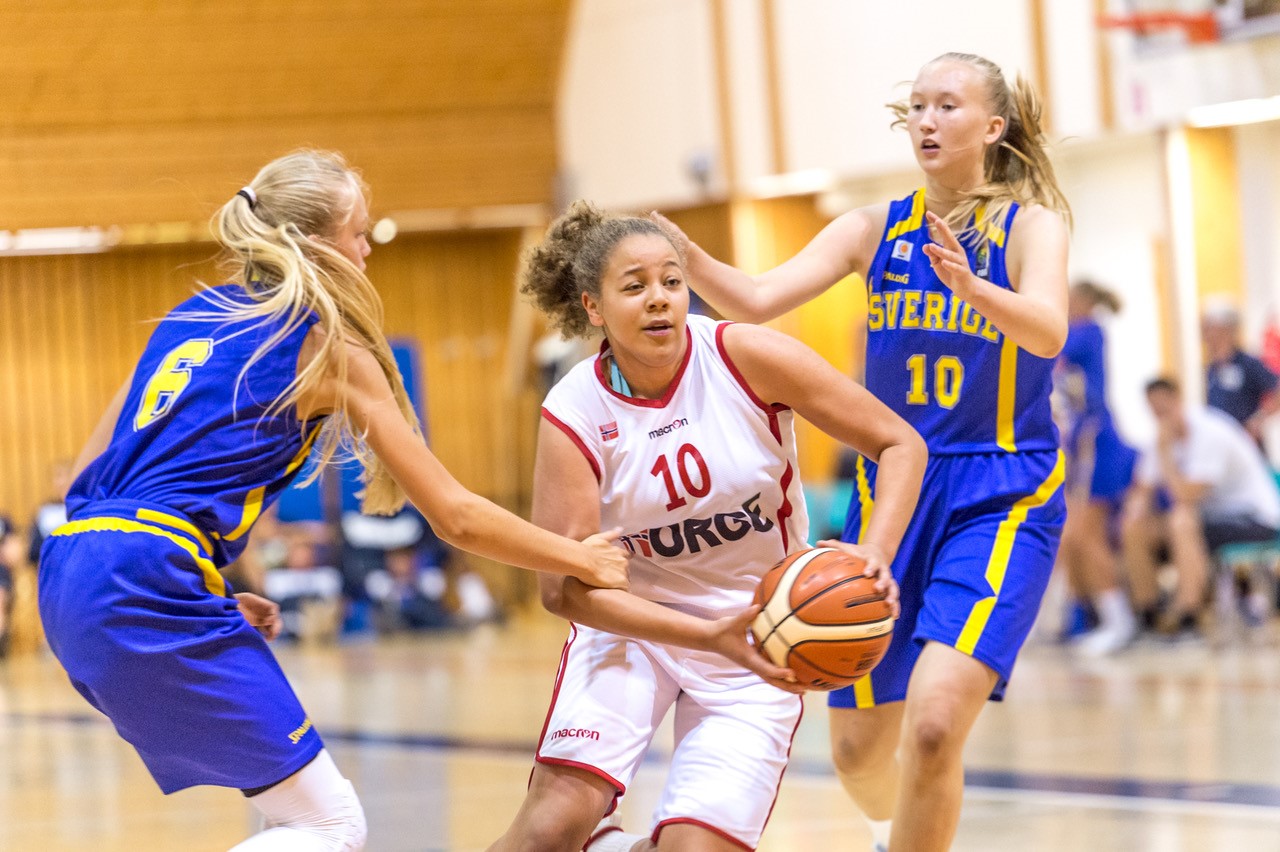 I 2018 sjokkerte Norges U16-jenter med de underårige 03-spillerne Sverige og vant 45-43, anført av Karyn Sanford (den gang 14 år) som her driver mellom to svenske spillere. Året etter ble det tap mot svenskene (56-62), men Norge vant sine fire øvrige kamper og sikret sølv i nordisk – og Sanford ble kåret til mesterskapets MVP.

FOTO: ASTRID HAGLAND GJERDE 
