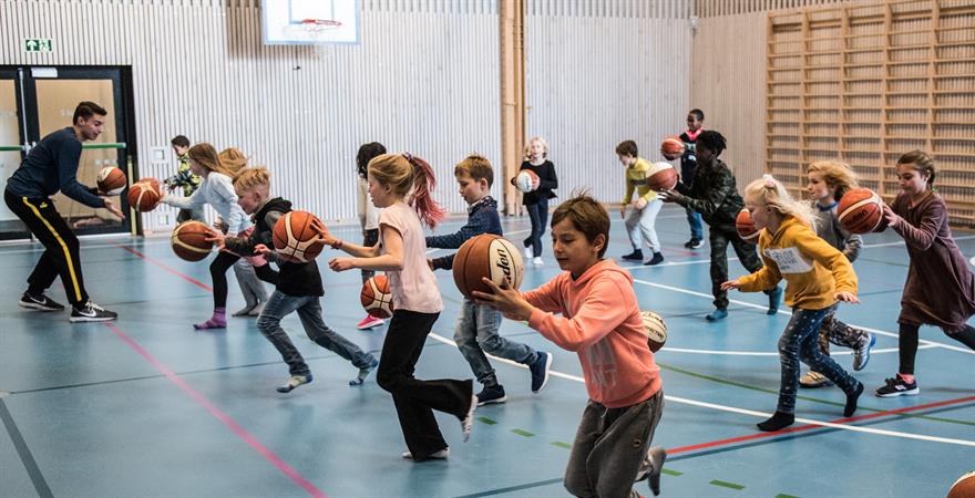 Tredje- og fjerdeklassinger ved Fernanda Nissen skole setter fart med ballen. Centrum Tigers-spiller Giorgos Kotrotsios til venstre i bildet er trener sammen med Inge-Aleksander Kristiansen.