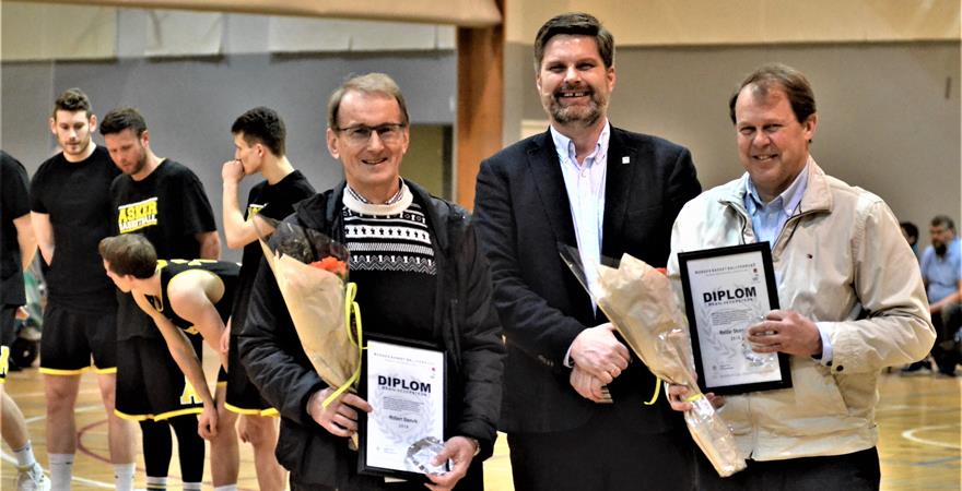 ​Robert Stenvik (til venstre) og Reidar Skorpen med Norges Basketballforbunds Hederstegn og hver sin blomsterbukett, med prisutdeler og NBBF-president Jan Hendrik Parmann i midten.